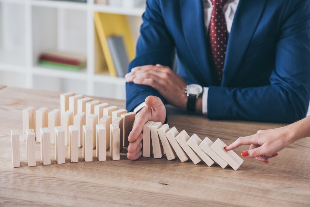 cropped view of woman pushing wooden block and risk manager stopping domino effect